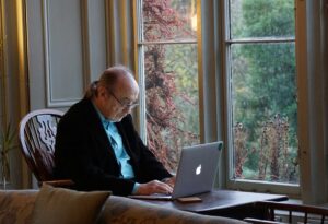 An elderly man sits and uses a computer.